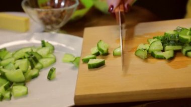 Bir kadın bir bıçakla dilimlenmiş salatalık beyaz bir tabak içinde koyar.