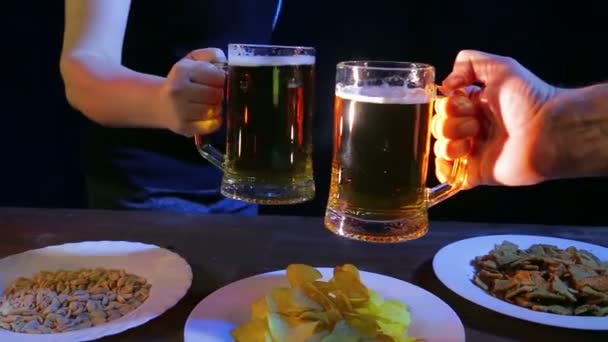 Las manos de los amigos en el bar golpearon tazas de cerveza juntos sobre un fondo negro — Vídeos de Stock