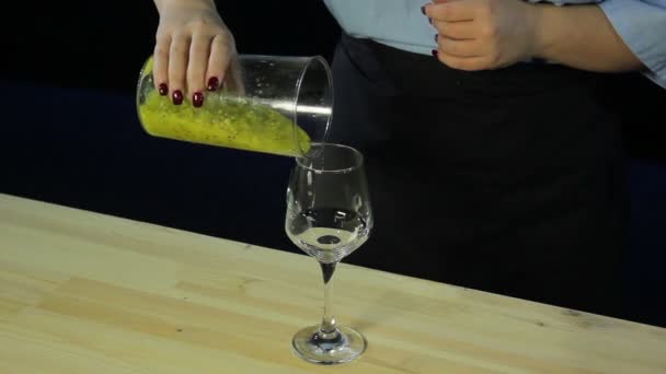 Une femme verse du kiwi et de la mangue déchiquetés dans un smoothie dans un gobelet de verre . — Video