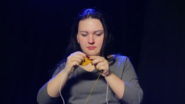 一个年轻的黑发女人在一个黑色的背景编织在圆形针织针从黄色线 — 图库视频影像