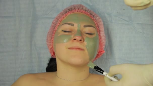 Мужчина-косметолог в перчатках надевает маску с кистью на лице клиентки — стоковое видео