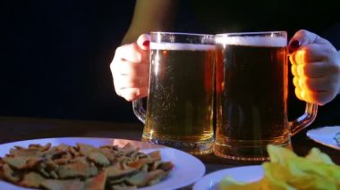 Barmen bir siyah arka plan iki tam kupalar köpük bira üzerinde atıştırmalıklar ile masanın üzerine koyar