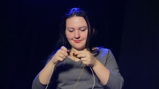 Een jonge brunette vrouw op een zwarte achtergrond breit op rondbreinaalden breien van gele draad — Stockvideo