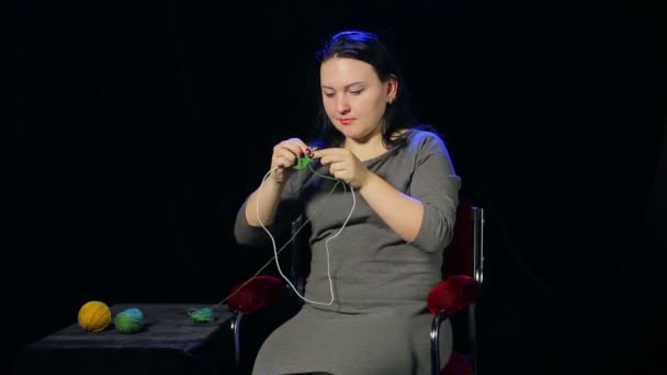 Een jonge brunette vrouw op een zwarte achtergrond breit op de naalden van groene draad — Stockvideo