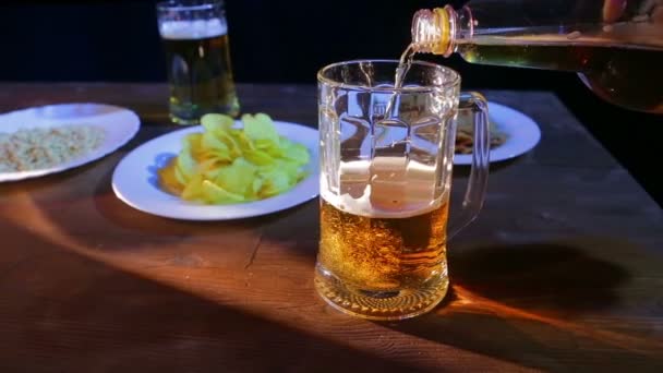 Licht schuimend bier wordt gegoten in een glazen mok op een houten tafel tegen een zwarte achtergrond — Stockvideo