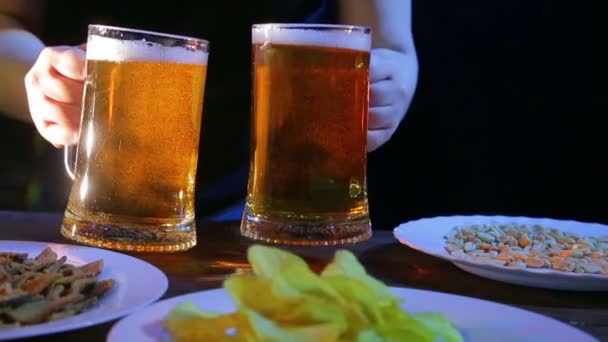 Una camarera pone en una mesa con bocadillos sobre un fondo negro dos tazas llenas de cerveza espumosa — Vídeos de Stock