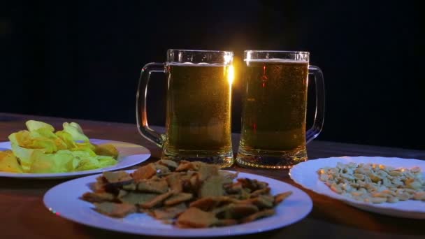 Mokken met schuimende light bier op een houten tafel tegen een zwarte achtergrond — Stockvideo