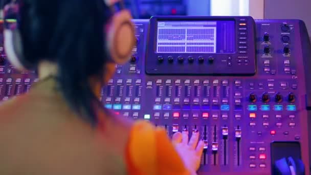 Mujer DJ en auriculares detrás de una consola de mezcla trabajando en iluminación de color . — Vídeos de Stock