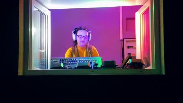 Mujer DJ en auriculares en la sala de radio tiene una discoteca en la consola de mezcla — Vídeos de Stock
