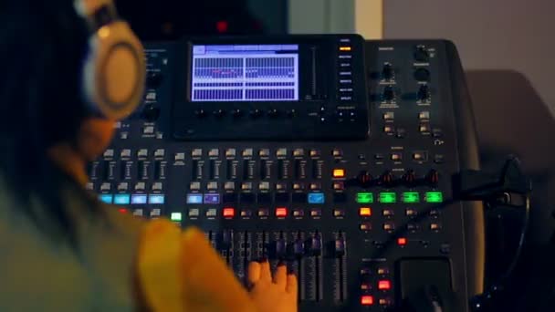 Donna DJ in cuffia dietro una console di miscelazione che lavora nell'illuminazione a colori — Video Stock