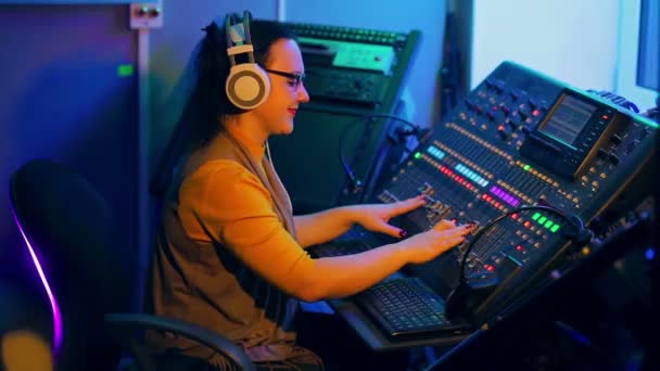 Vrouw in hoofdtelefoons en glazen mixen tracks voor disco op een mengpaneel — Stockvideo