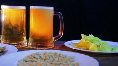 Bira bardağı köpük bira atıştırmalıklar ile ahşap bir masa üzerinde siyah bir arka plan ile