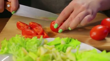 Kadın bir kiraz domates bir ahşap tahta üzerinde bir bıçakla keser. Yakın çekim