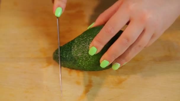 Ženská ruka čistí avokádo ovoce s nožem na dřevěném prkénku. — Stock video
