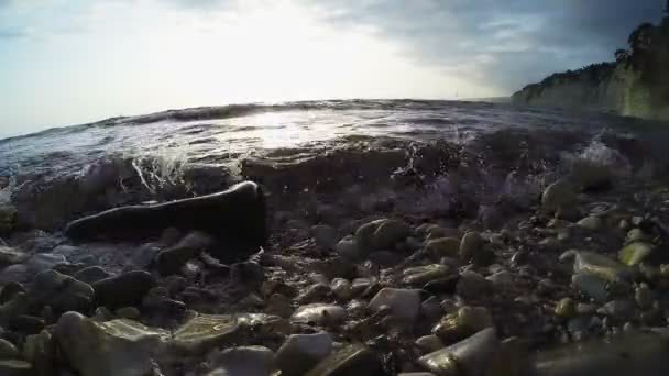 Köves tengerparton napnyugtakor a nap kiemeli a sziklák — Stock videók