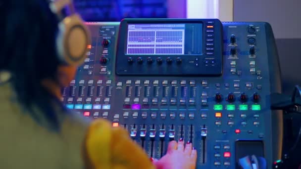 Donna DJ in cuffia dietro una console di miscelazione che lavora nell'illuminazione a colori — Video Stock