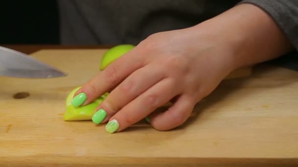 Een vrouw snijdt een groene appel met een mes op een houten plank in kleine blokjes — Stockvideo