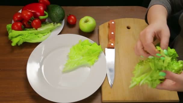 Uma mulher coloca folhas de alface verde em um prato branco — Vídeo de Stock