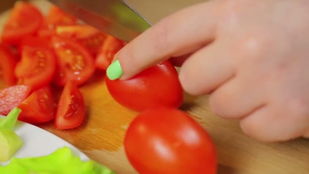 La mano femenina corta un tomate cherry con un cuchillo en una tabla de madera . — Vídeos de Stock