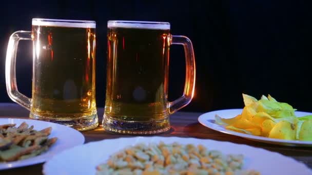 Bierkrüge mit Schaumbier auf schwarzem Hintergrund auf einem Holztisch mit Snacks — Stockvideo