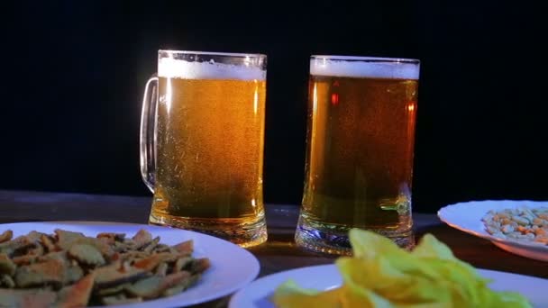 Tazas con cerveza ligera espumosa sobre una mesa de madera sobre un fondo negro . — Vídeos de Stock