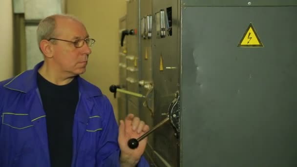 En elektriker ingenjör höjer handtaget och vänder på den elektriska panelen — Stockvideo
