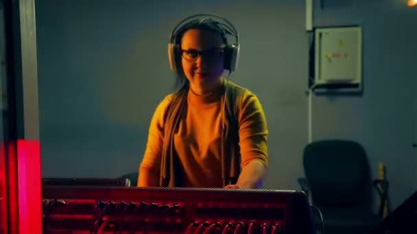 Un DJ donna con le cuffie in un locale tecnico conduce una discoteca su una console di mixaggio alla luce di una discoteca — Video Stock