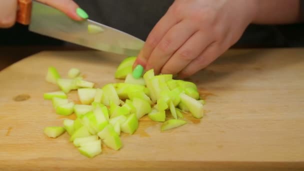 Una mujer corta una manzana verde con un cuchillo en una tabla de madera en cubos pequeños . — Vídeo de stock