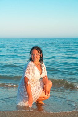 Genç bir kadın beyaz dantel pelerin kıyı dalgalar deniz kum üzerinde oturuyor.