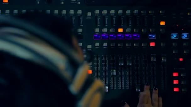 在调音台后面的耳机中工作的女性 Dj 在彩色照明 — 图库视频影像
