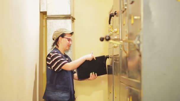 Жінка-інженер-електрик записує показання електричних приладів у щиті — стокове відео