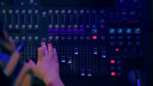 Mãos das mulheres em um console de mistura misturando faixas para discoteca em iluminação colorida — Vídeo de Stock