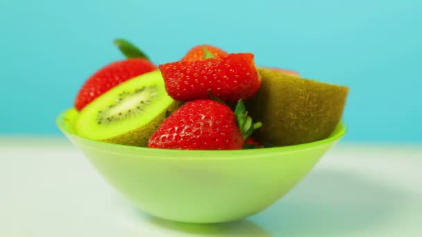 O fruto fresco de quivi e morangos fatiados em um contexto azul em uma chapa verde gira em um círculo — Vídeo de Stock