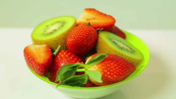 Nakrájené jahody na modrém pozadí na zelené štítku a čerstvé kiwi se otáčí v kruhu. Pohled shora — Stock video