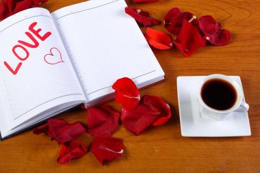 Bir fincan kahve ve bir günlük kırmızı ahşap bir masa üzerinde kelime aşk ile.