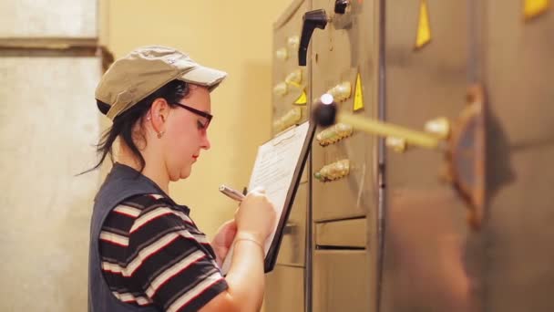 A female engineer writes down the readings of electrical appliances in the switchboard — Stock Video