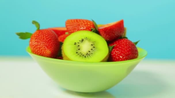 Свіжі фрукти ківі і нарізані полуниці на синьому фоні на зеленій тарілці обертаються в колі — стокове відео