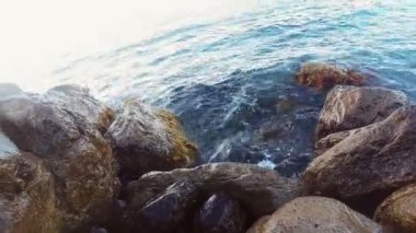 Kayalık deniz kıyısı ve akşamları güneş ışığı altında taşlar karşı çökmesini dalgalar