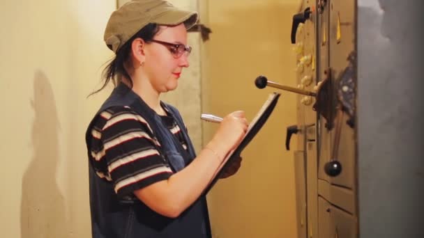 En kvinnlig ingenjör registrerar instrument avläsningarna i elektriska rummet — Stockvideo