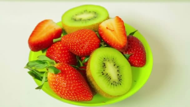 Νωπά ακτινίδια και φράουλες σε φέτες σε ένα μπλε φόντο σε ένα πιάτο περιστρέφεται σε έναν κύκλο. Θέα από ψηλά. — Αρχείο Βίντεο