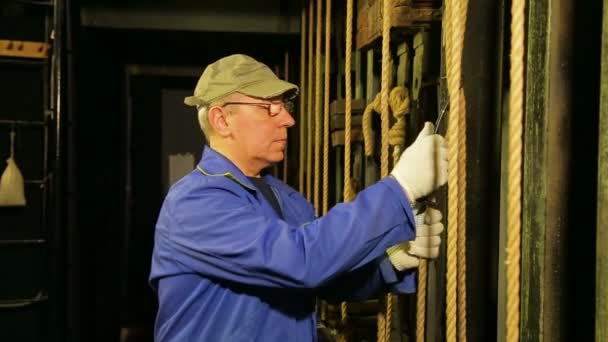 De werknemer van de etappe in handschoenen verwijdert van de berg van de kabel van het hefmechanisme van de theater-gordijn en verlaagt het. — Stockvideo