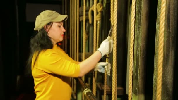 Bir genç kadın sahne işçi eldiven mount bir tiyatro perde mekanizması kaldırma bir kablo kaldırır. — Stok video