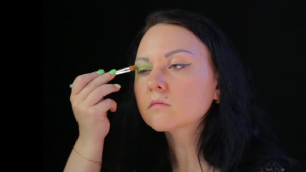 En brunett kvinna gör ögonmakeup med gröna skuggor framför en spegel. — Stockvideo