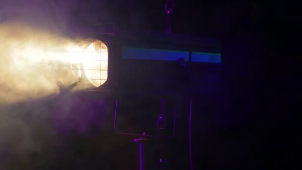 Un haz luminoso de un proyector de perfil teatral giratorio en las nubes de humo frío en el escenario — Vídeos de Stock