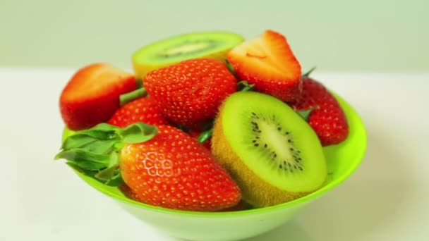 Färsk kiwi och skivade jordgubbar på en blå bakgrund på en grön platta roterar i en cirkel. Visa från ovan — Stockvideo