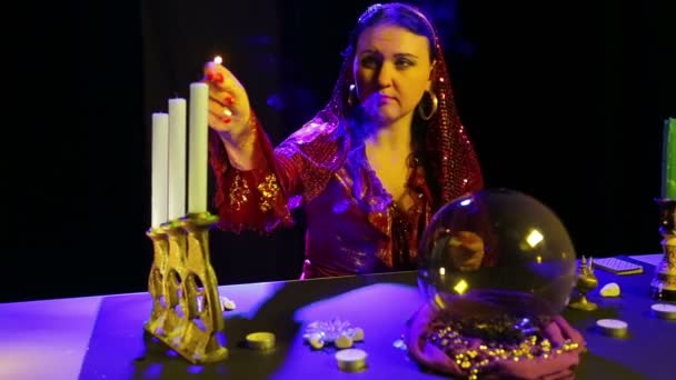 Gypsy in a red dress in a scarf lights candles in an old candlestick — Stock Video