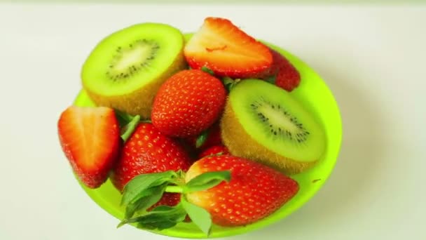 Fresh kiwi and sliced strawberries on a blue background on a plate rotates in a circle. View from above — Stock Video