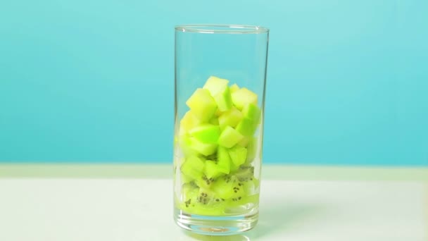 У прозорому склі нарізані скибочки фруктів ківі та яблука. Скло обертається в колі — стокове відео