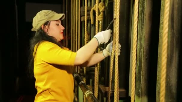 Сценическая работница в перчатках прижимает трос, чтобы поднять театральный занавес — стоковое видео
