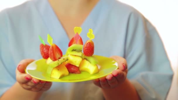 A mulher - o chef sorri e mantém um prato com uma sobremesa de fruto nas mãos. Controle a luz solar da janela . — Vídeo de Stock
